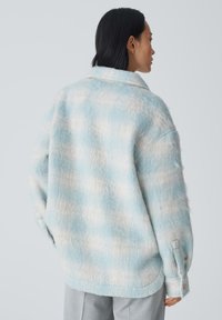 Veste en chemise à motif flou en bleu clair et crème. Dotée d'un col, de poignets à bouton et d'une coupe ample pour plus de confort. Texture douce.