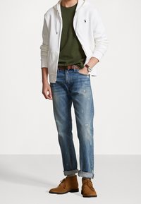 Vit zip-up hoodie, olivgrön T-shirt, slitna ljusblå jeans, bruna ankelboots, brunt bälte, silverfärgad klocka, avslappnad stil.