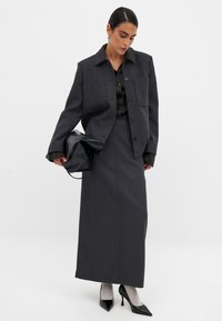 Sivi krojeni sako z dvema žepoma na prsih, v kombinaciji z dolgim krilom v istem odtenku. Črne čevlje z visokimi petami, prosojne nogavice in črna torbica.