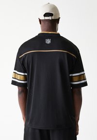 Black NFL jersey with gold and white stripes on sleeves, mesh texture, and NFL logo at the back neck. Back view shows design details.