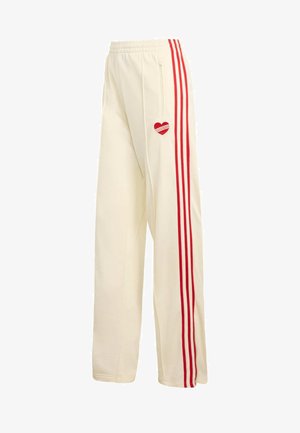 Cream-colored sweatpants with red stripes down the sides, featuring a red heart logo on the left thigh and a side zip pocket.