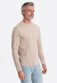 Långärmad beige bomullströja med rund halsringning, lätt stretch och en slät yta. Bärs med ljusblå jeans.