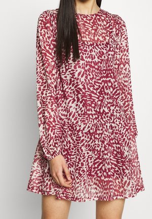 Vrouw draagt een lange mouw, boven-de-knie jurk met een rood-wit abstract dierenprintpatroon.