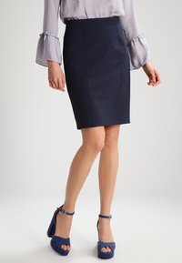 Mörkblå blyertkjol med en slank design, som har en jämn textur och en figurnära silhuett, tillsammans med blåa mockahögklackade skor.