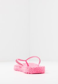 Vaaleanpunaiset flip-flopit, joissa on kudottu muotoilu, ja niissä on teksturoitu pohja sekä ohuet, kaarevat remmit. Pohjassa on punottu ulkonäkö.