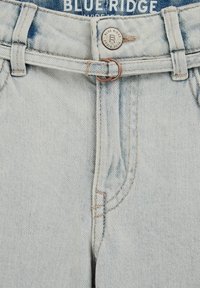 Svetlo pranje denim kavbojk s širokimi nogavicami, ki imajo bronast gumb, pas z zanko in okroglim obročkom ter subtilno zbledelost na tkanini.
