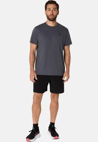 Grå kortærmet t-shirt med rund halsudskæring, parret med sorte træningsshorts og sorte løbesko med pink accenter.