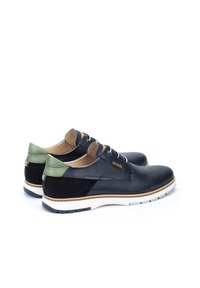 Chaussures en cuir noir avec une finition texturée, accents verts au talon et semelle en caoutchouc blanche. Panneaux latéraux perforés et détails cousus.