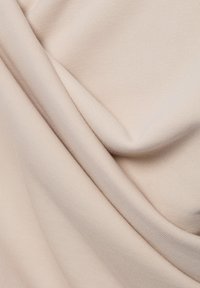 Tessuto beige chiaro con una texture liscia e a coste, che mostra pieghe morbide e cadenti, evidenziando il materiale leggero e flessibile.