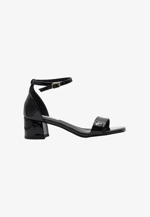 Sandalo in pelle verniciata nera con tacco largo, cinturino alla caviglia, chiusura con fibbia e design con punta aperta.
