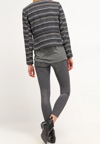 Černošedý pruhovaný zkrácený kabát přes šedé tričko, spárovaný s tmavě šedými skinny džíny a černými kotníkovými botami.