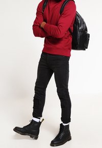 Röd sweatshirt, svarta slitna jeans och svarta ankelskor. Tillbehören inkluderar en svart läderryggsäck. Enkel och funktionell design.