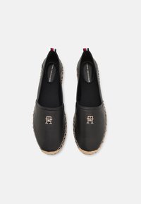 Espadrilles noires à enfiler avec semelles en jute tressé et logo Tommy Hilfiger argenté sur le dessus, vues de dessus sur un fond blanc.
