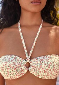 Krēmkrāsas ziedu bikini tops ar roz�ā ziediem, ar sasietu centru un plānām siksnām. Tekstūrēta auduma ar rautiņu detaļām.