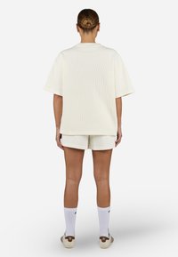 Top corto a maniche lunghe color crema a coste abbinato a pantaloni corti coordinati, accentuato da calzini bianchi e sneaker in tonalità neutre.