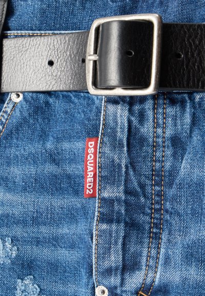 Gros plan sur un jean en denim bleu avec une étiquette rouge DSQUARED2 et une ceinture en cuir noir avec une boucle rectangulaire argentée.