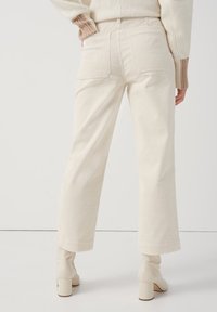 Pantalones de pana crema con perneras rectas, bolsillos delanteros y costuras visibles. Combinados con botas de tobillo de tacón cuadrado pálido.