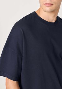 Temno modra bombažna majica z okroglim izrezom in kratkimi rokavi, ki ima sproščen kroj in gladko teksturo.