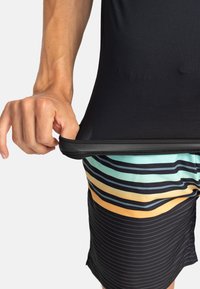 Svart atletisk topp med rundad nederkant, bärs över flerfärgade randiga badshorts med horisontella ränder i teal, orange och svart.