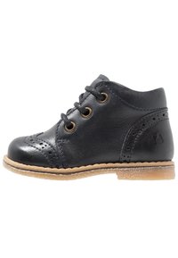 Stivale alla caviglia in pelle nera con dettagli brogue, punta rotonda, chiusura con lacci e suola in gomma marrone chiaro. Texture liscia con finitura lucida.
