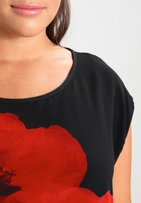 Černý top s velkým červeným květinovým potiskem, kulatým výstřihem a krátkými rukávy. Hladká látka s drapérií, neformální design.