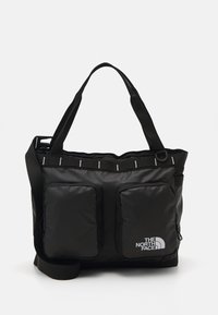 Saco tote preto em nylon com dois bolsos frontais com fecho zip, fechamento superior com zipper e uma alça de ombro ajustável. Apresenta detalhes refletivos.