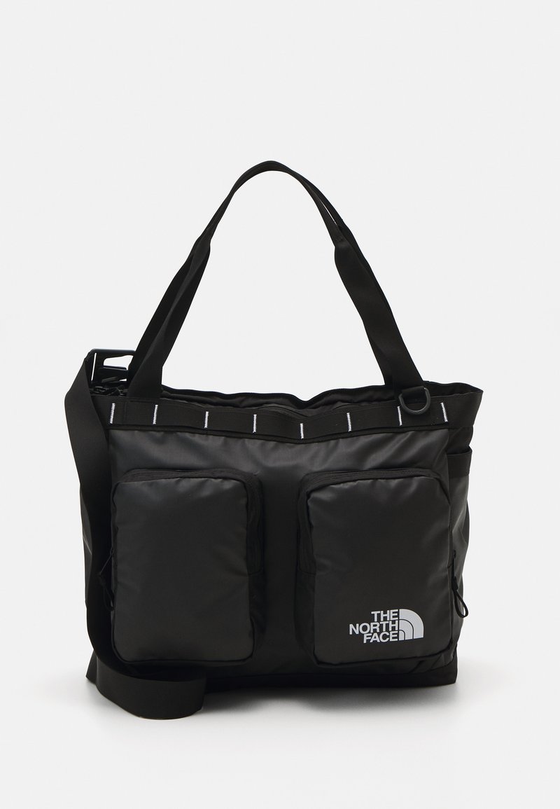 Saco tote preto em nylon com dois bolsos frontais com fecho zip, fechamento superior com zipper e uma alça de ombro ajustável. Apresenta detalhes refletivos.