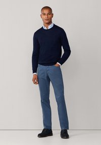 Marineblauwe wollen trui met ronde hals, lichtblauw overhemd eronder, gecombineerd met slim-fit blauwe broek en zwarte suède schoenen.