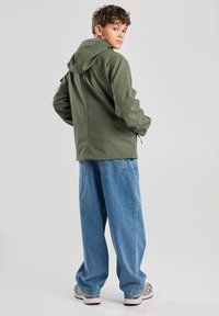 Green hooded jacket made of soft fabric, featuring a relaxed fit. Paired with loose light blue denim pants and sneakers.