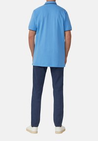 Light blue short-sleeve polo shirt features a classic collar and trim, paired with navy pants and white sneakers, showcasing a relaxed fit.