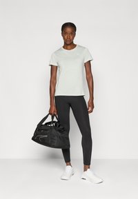 Világoszöld, rövid ujjú póló, fekete leggings és fehér sportcipő. Fekete sporttáska hálós panellel és díszítéssel.