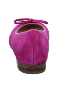 Zapato plano de ante magenta con punta redondeada, un delicado lazo en la parte delantera y una suela marrón texturizada y baja. Vista trasera, textura lisa.
