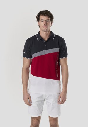 Camiseta tipo polo a rayas azul marino y rojo con detalles en gris. Cuenta con una tapeta de dos botones y un dobladillo blanco. Se combina con pantalones cortos blancos remangados.