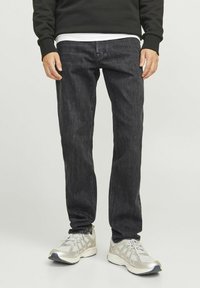 Jeans de mezclilla oscura con un corte recto, que presentan una textura sutil y un diseño clásico de cinco bolsillos. Combinados con zapatillas deportivas de color plata claro.