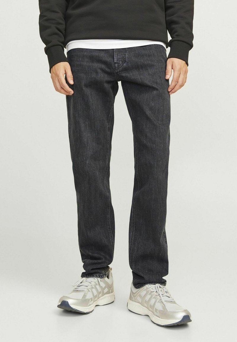 Jeans de mezclilla oscura con un corte recto, que presentan una textura sutil y un diseño clásico de cinco bolsillos. Combinados con zapatillas deportivas de color plata claro.