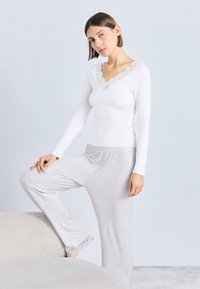 Biele tričko s dlhým rukávom a čipkovaným výstrihom, skombinované so svetlosivými nohavicami s čipkovými detailmi na leme, oboje z jemnej, textúrovanej látky.