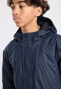 Navy blue, lightweight, hooded jacket with a zip front and snap buttons. Features a smooth nylon texture and subtle stitching details.