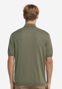 Kortärmad, olivgrön polo med mjukt stickat material. Har en klassisk krage och ribbade muddar, med en ren och enkel design.