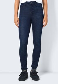 Mörkblå högmidjade skinny jeans med en slät yta och minimal detaljering, kombinerat med svarta sneakers med en logotyp.