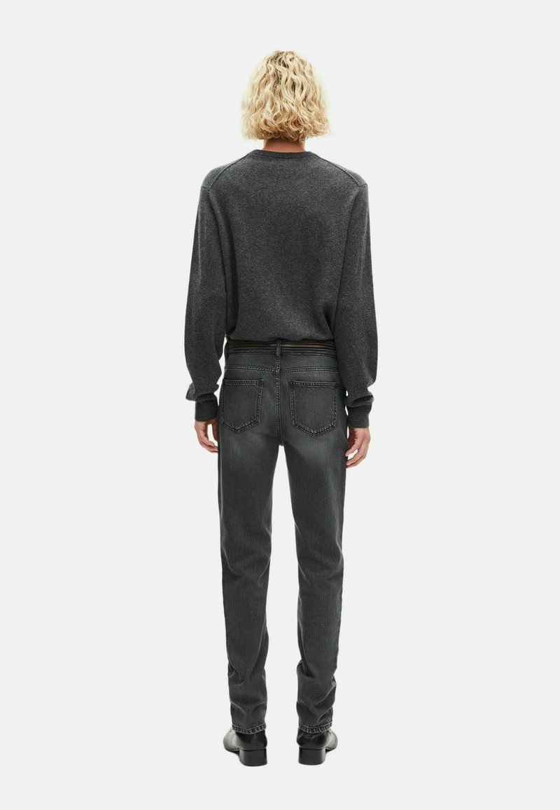Dunkelgrauer Langarmpullover und schmal geschnittene dunkle Jeans. Der Pullover hat einen runden Halsausschnitt und überschnittene Schultern; die Jeans verfügen über Gesäßtaschen und einen Bund.