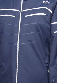 Mörkblå jacka med främre dragkedja, prydd med horisontella vita ränder och subtila texturerade detaljer. Inkluderar fickor och varumärkeslogotyp.