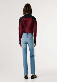 Riba särke tumesinises ja punases, millel on logo detail taga, koos helesiniste sirgete lõikega teksade ja mustade kingadega.