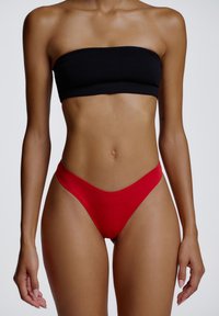 Haut bandeau noir et bas de bikini taille haute rouge, tissu lisse, coupe ajustée, couvrance minimale, pas de motifs ni de détails visibles.
