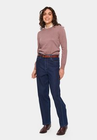 Mörkblå denimjeans med raka ben, utrustade med bältesöglor och sidofickor, som bärs tillsammans med en ljusbrun långärmad tröja.