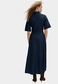 En denim skjortekjole i mørkeblå, med korte ærmer, en figursyet talje og en svævende lang nederdel med et lagdelt design.