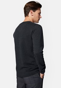 Sweter w kolorze węgla, z prążkowanymi mankietami i dołem, o drobno dzianym wykończeniu, z okrągłym dekoltem, dopasowany krój, noszony z wzorzystymi spodniami.