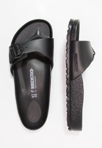 Sandale negre Birkenstock cu curea ajustabilă, talpă texturată și talpă cu striații. Prezintă logo embosat și detalii de mărime în interior.