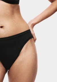 Zwarte bikini onderkant met een lage taille, voorzien van gladde stof en een minimalistische snit die comfort en eenvoud benadrukt.