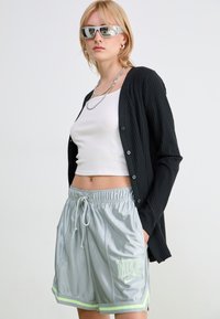 Black ribbed cardigan, white tank top, and silver Nike shorts with neon green accents. Model wears reflective sunglasses and silver jewelry.