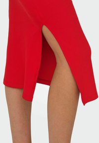 Abito rosso a coste con dettaglio di alta slit sul lato sinistro. Il tessuto presenta una texture liscia, con un design aderente che segue la forma del corpo.